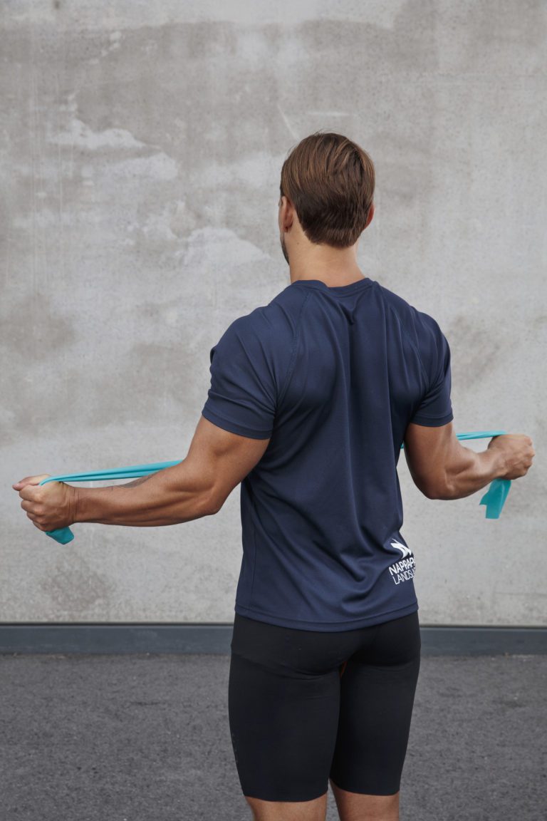 Bilden visar en man som tränar skuldrornas utåtrotatorer med hjälp av ett gummiband